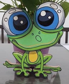 a green frog sitting on top of a table next to a potted plant