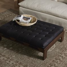 a black ottoman sitting on top of a rug in front of a couch and coffee table