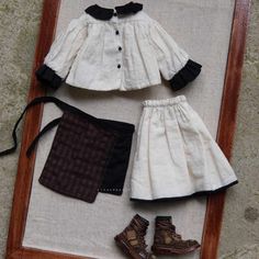 an old fashion doll is displayed in a wooden frame with shoes and clothing on the floor