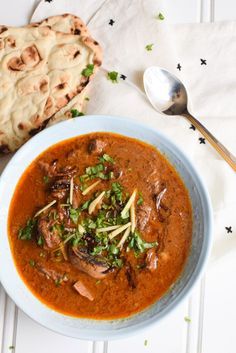 a bowl of soup next to a piece of bread on a white tablecloth and spoon