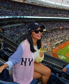 a woman sitting in the bleachers at a baseball game wearing sunglasses and a new york yankees jersey