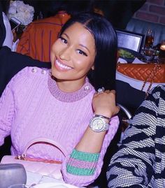 a woman sitting at a table with a pink purse on her lap and smiling for the camera