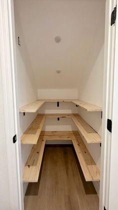 an empty white room with wooden benches in the corner and hard wood flooring on both sides