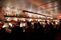 a group of people sitting at a bar with liquor bottles on the shelves behind them