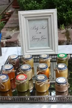 there are many jars of jams on the table with a framed picture behind them