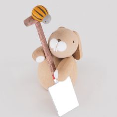 a teddy bear holding a wooden stick with a bee on it's back and a blank sign in its hand