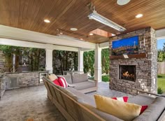 an outdoor living area with couches, fireplace and flat screen tv on the wall