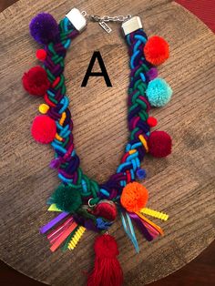 a multicolored necklace with pom - poms on it and the letter a