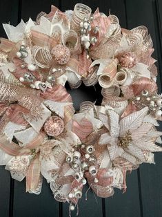 a pink and white wreath with pearls, bows and ribbons on a black wooden door