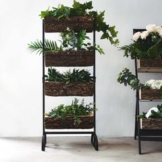 three plant stands with plants in them and flowers on the top one is filled with greenery