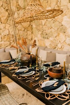 a table set with plates and place settings in front of a stone wall behind it