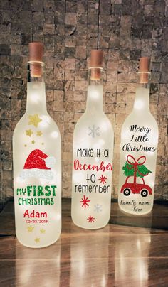 three bottles with christmas designs on them sitting next to each other in front of a brick wall