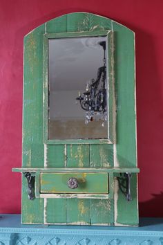 an old green wooden mirror on top of a blue shelf