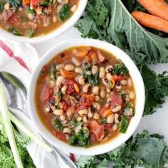 two white bowls filled with beans, carrots and greens on top of a table