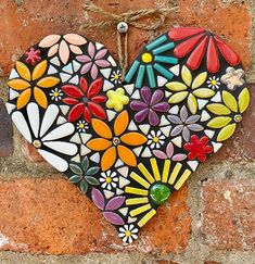 a heart shaped decoration hanging on a brick wall with flowers and leaves painted on it