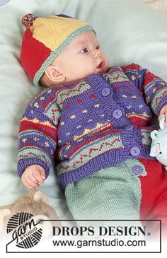 a baby laying on top of a bed next to a teddy bear wearing a knitted hat