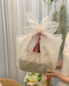 a woman is holding a large basket with a bow on it and flowers in the background