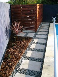 a small garden area next to a pool with rocks and gravel on the ground, along with a wooden fence