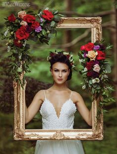 a woman in a wedding dress holding up a frame with flowers around her neck and hands