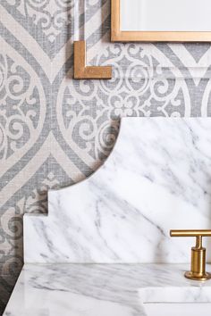 a marble sink with gold faucet in front of a wallpapered background