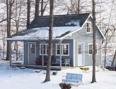 a small blue house in the woods with snow on the ground and trees around it