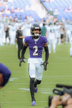 a football player is running on the field with his hands in his pockets as people are taking pictures behind him