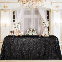 a black table cloth with white flowers and candles on it in front of a chandelier