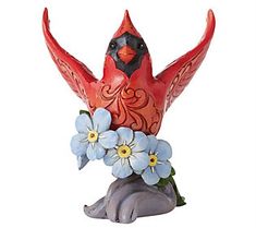 a red bird figurine sitting on top of a rock with blue and white flowers