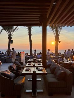 people are sitting at tables on the beach with palm trees in front of them and an ocean view