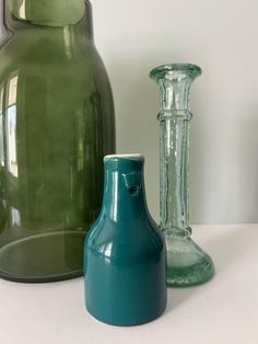 three different colored vases sitting on a white counter top, one is green and the other is blue