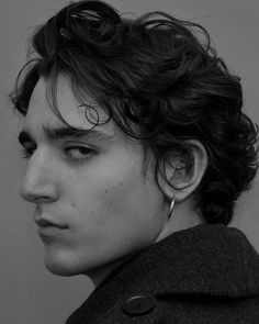 a young man with curly hair and piercings looks off to the side in black and white