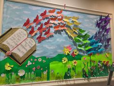 a bulletin board with colorful paper flowers and an open book in the middle, surrounded by butterflies