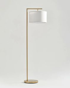 a floor lamp with a white shade on the top and a gold metal base, against a light gray background