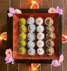 there are many different types of cupcakes in the tray on the table next to flowers