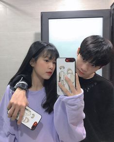 two people taking a selfie in front of a mirror with their cell phones up