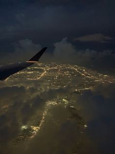 an airplane wing flying over the city lights in the night sky above clouds and land