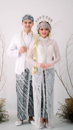 two people standing next to each other in front of white walls and plants wearing headdresses