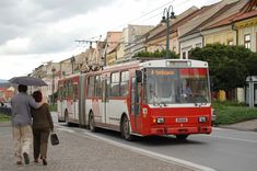 two people walking down the street with an umbrella in front of a red and white bus