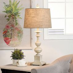 a table lamp sitting on top of a wooden table next to a chair and potted plant