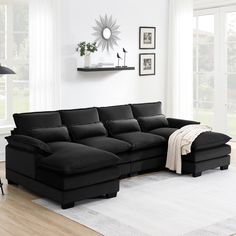 a living room with a black sectional couch and white rugs on the hardwood floor