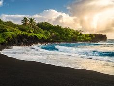 the sun shines brightly on an ocean beach with black sand and palm trees in the foreground