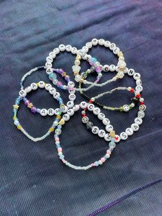 four bracelets with beads are laying on a blue fabric surface and one has a white beaded clasp