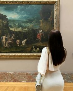 a woman sitting in front of a painting looking at it