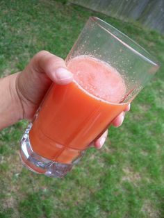 a person holding up a glass filled with orange juice on top of a grass covered field