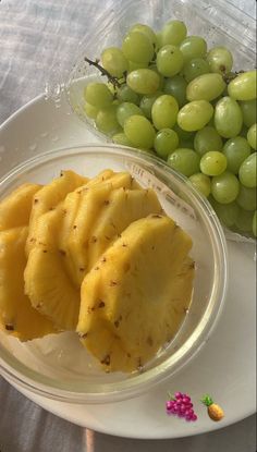 grapes and pineapple slices on a plate next to a bowl of green grapes in a plastic container