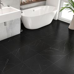 a white bath tub sitting next to a sink in a bathroom on top of a black tile floor