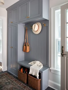 a gray bench with two baskets under it and a hat hanging on the coat rack