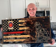 a man holding up a wooden plaque with an american flag and firefighter on it