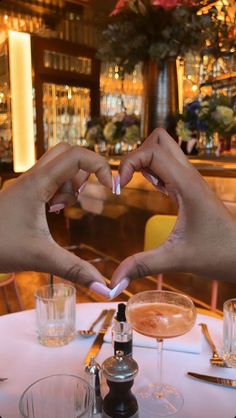 two hands making a heart shape with their fingers at a table in front of wine glasses