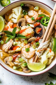 a bowl of shrimp noodle soup with chopsticks in it and lime wedges on the side